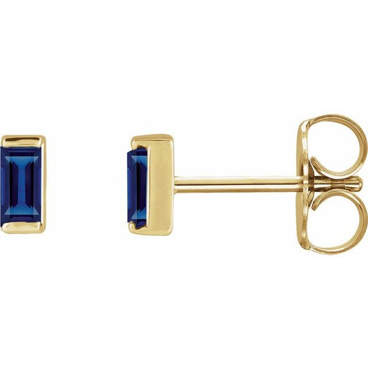 Gold earrings with baguette cut blue sapphire gemstones on a white background