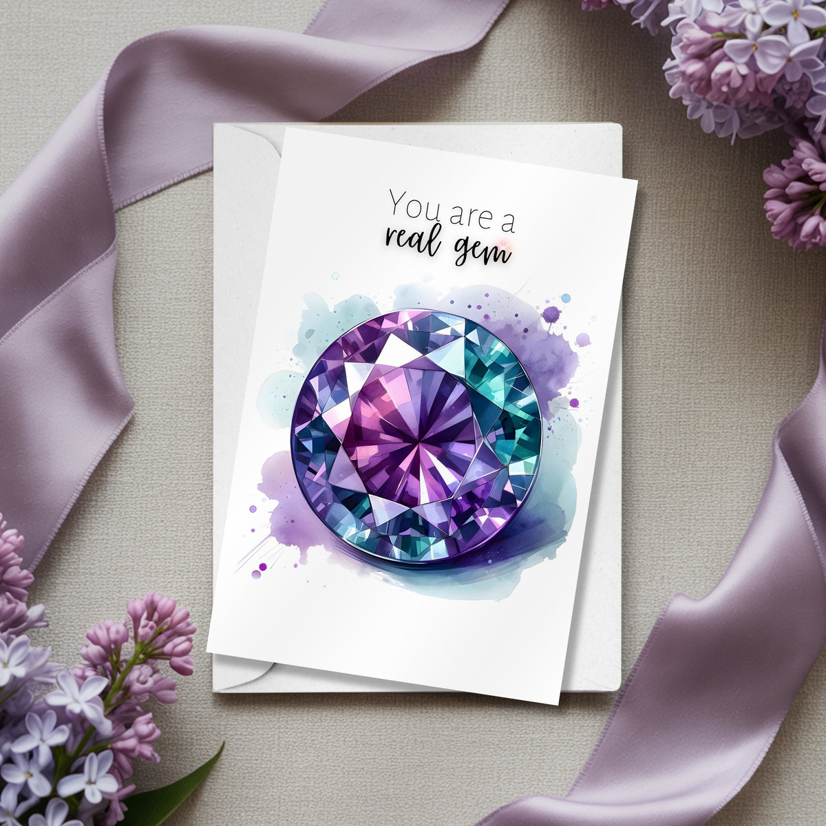 Greeting card with purple alexandrite watercolor illustration and text 'You are a real gem' on a beige surface with lilac flowers and ribbons.