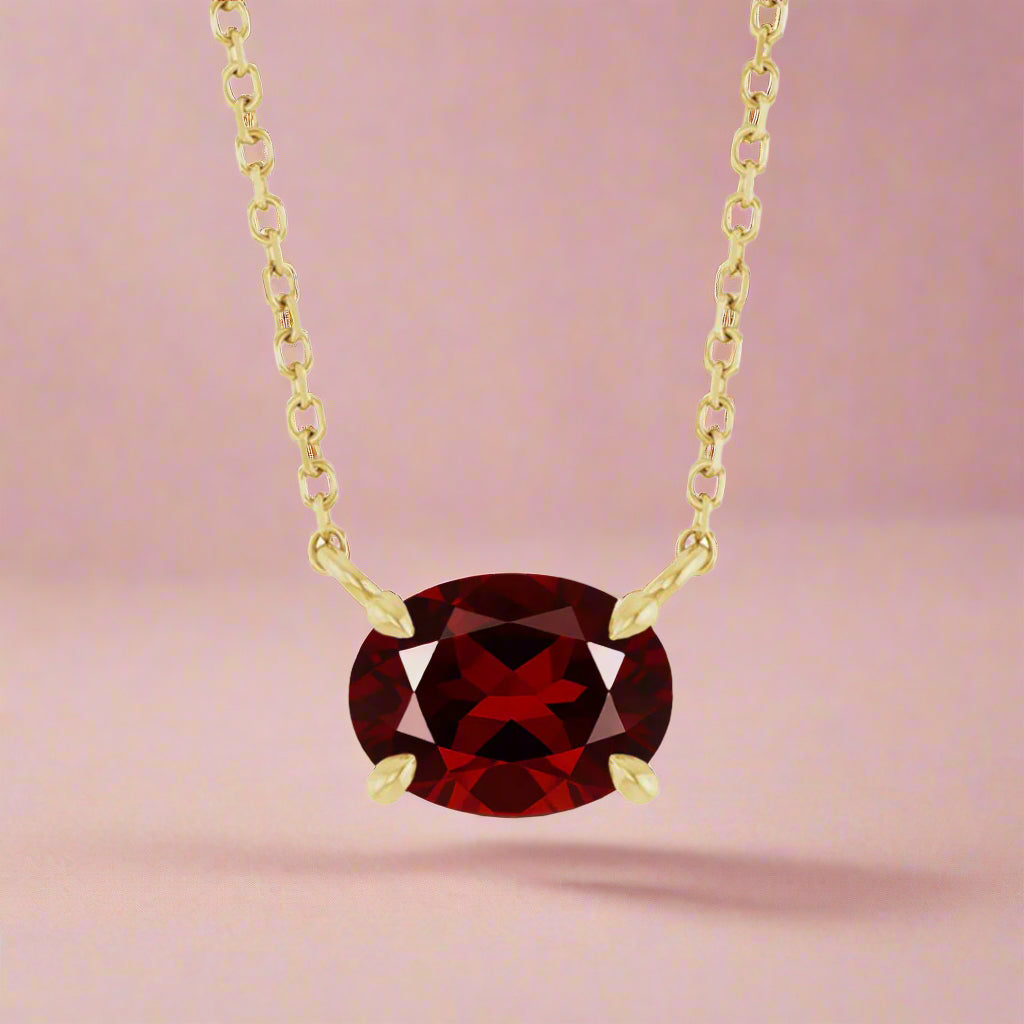 sideways set Oval Garnet Prong Set Birthstone gold Pendant Necklace on pink background