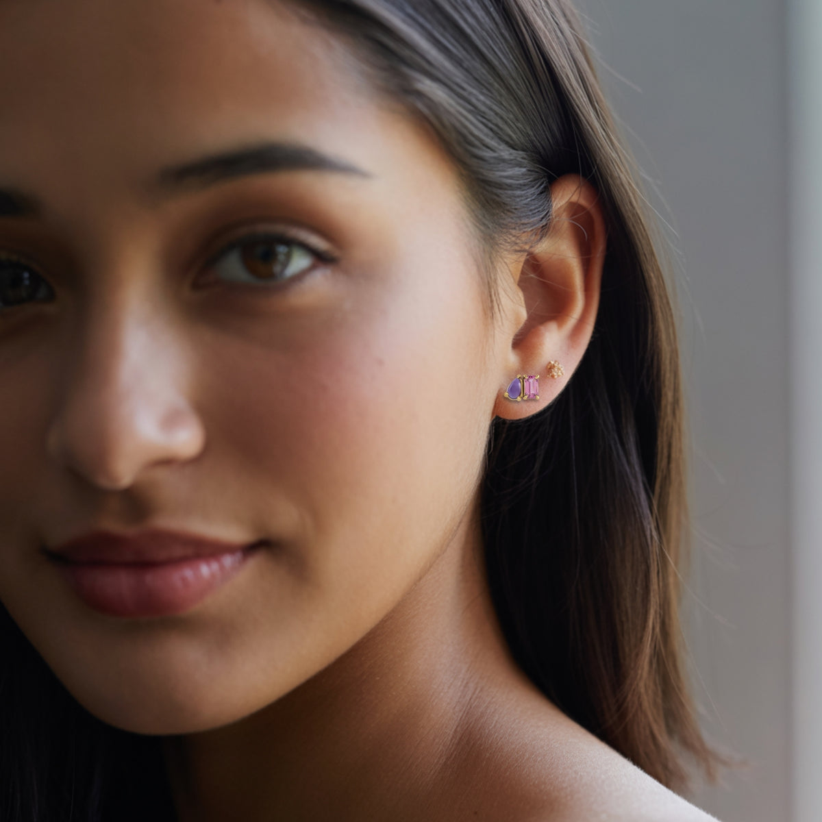 Emerald cut Pink Tourmaline & Pear Amethyst Two-Stone Birthstone Stud Earrings in gold on a woman's ear