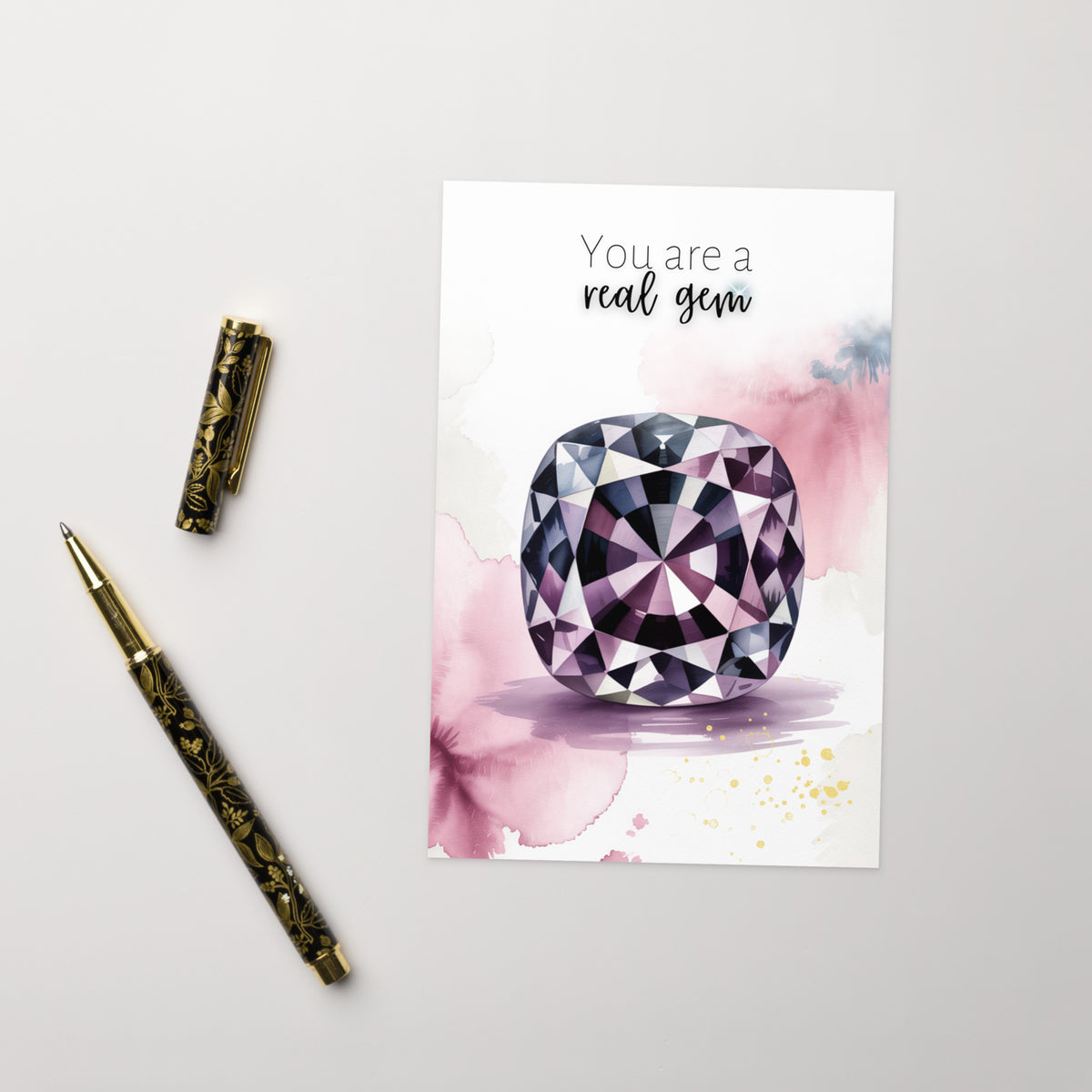 Greeting card with a purple spinel illustration and text 'You are a real gem' on a light gray background with a pen.