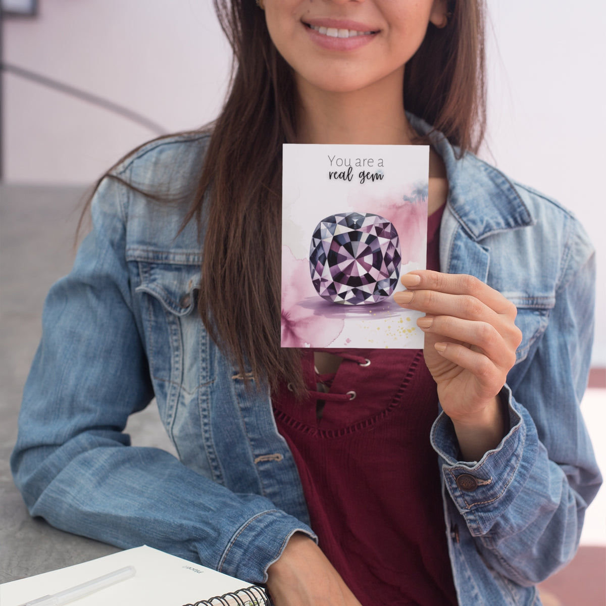 Person holding a card with a spinel illustration and text, wearing a denim jacket.