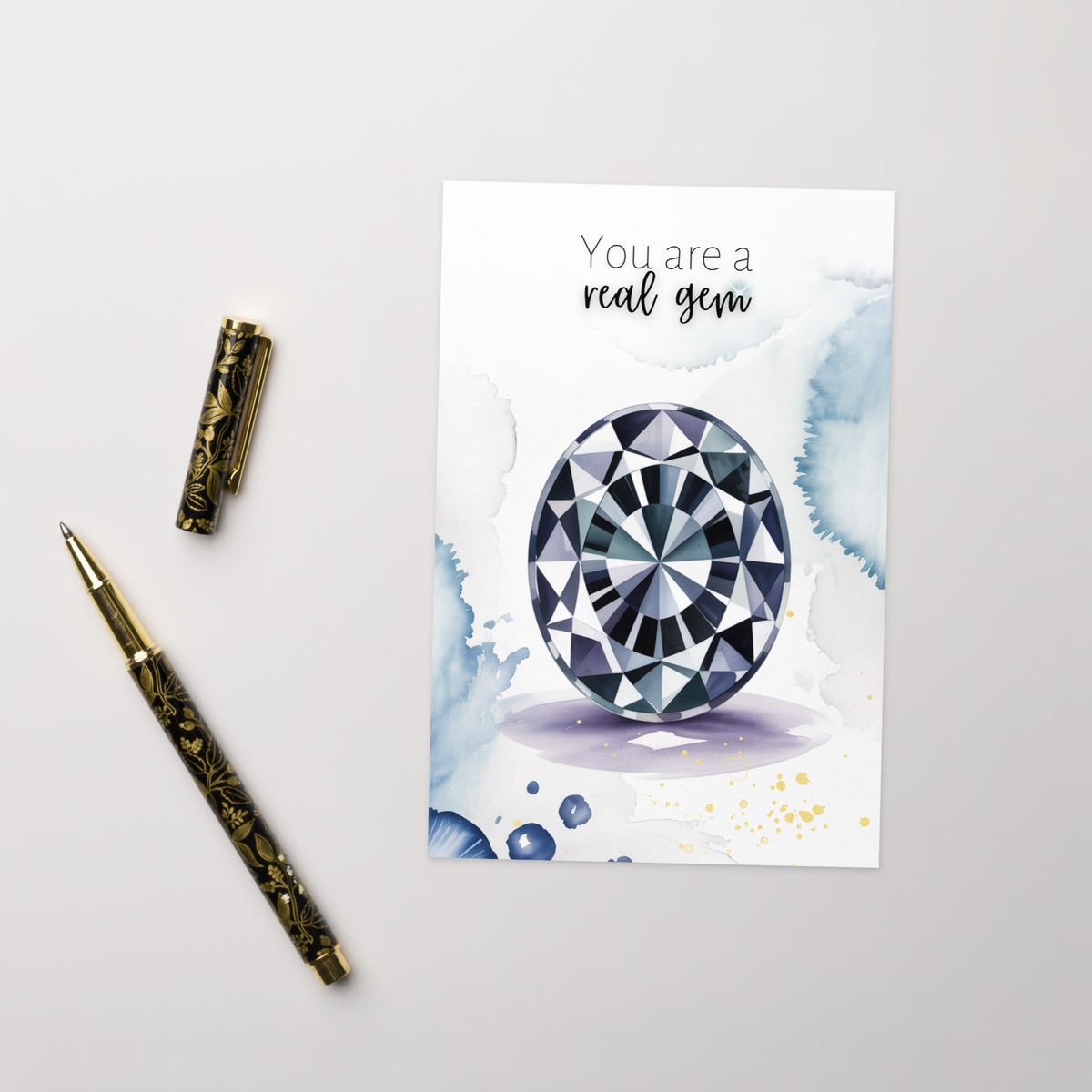 Greeting card with an oval Spinel Gemstone illustration and 'You are a real gem' text, accompanied by a pen on a light gray background.