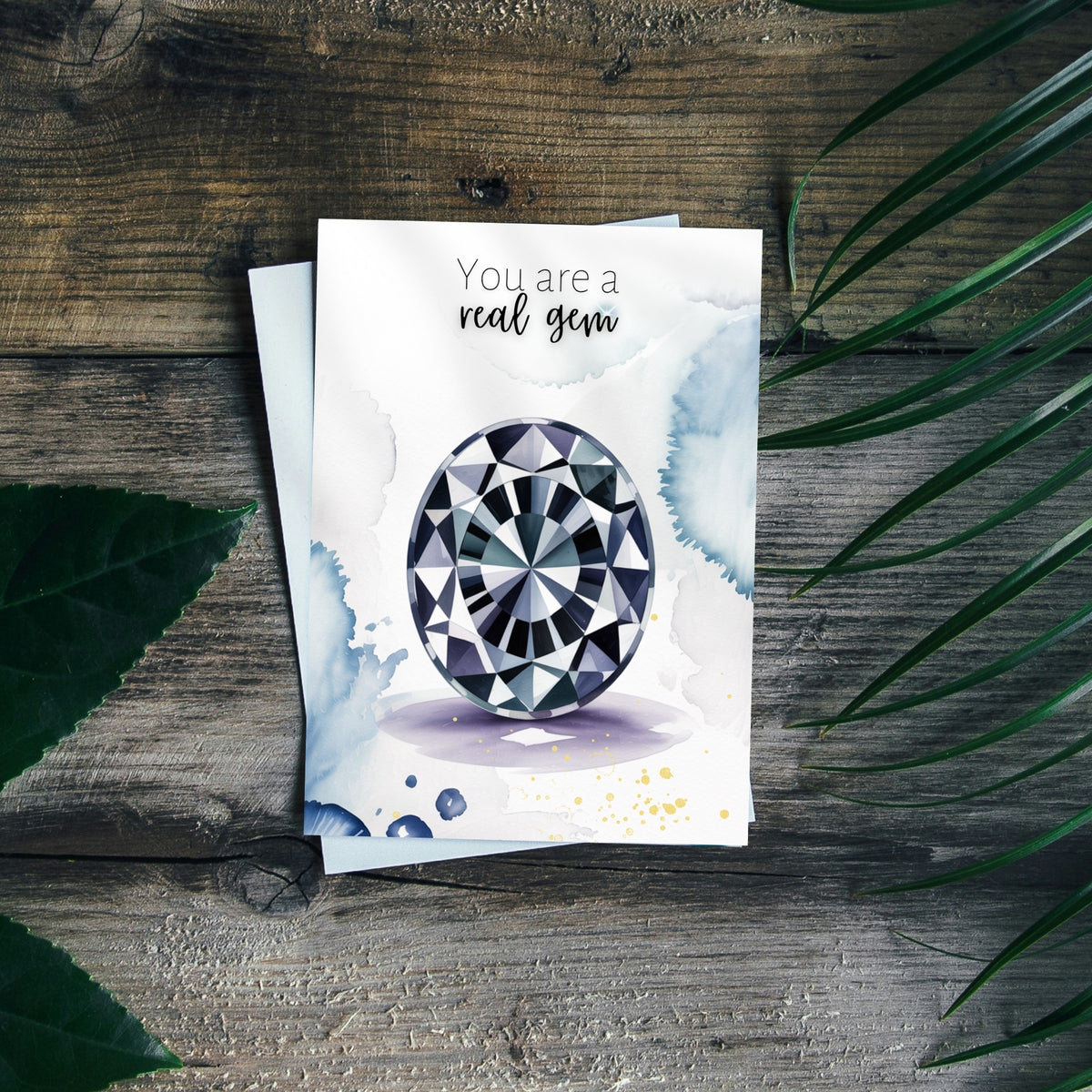 Greeting card with oval Spinel Gemstone illustration and text 'You are a real gem' on a wooden surface with leaves.