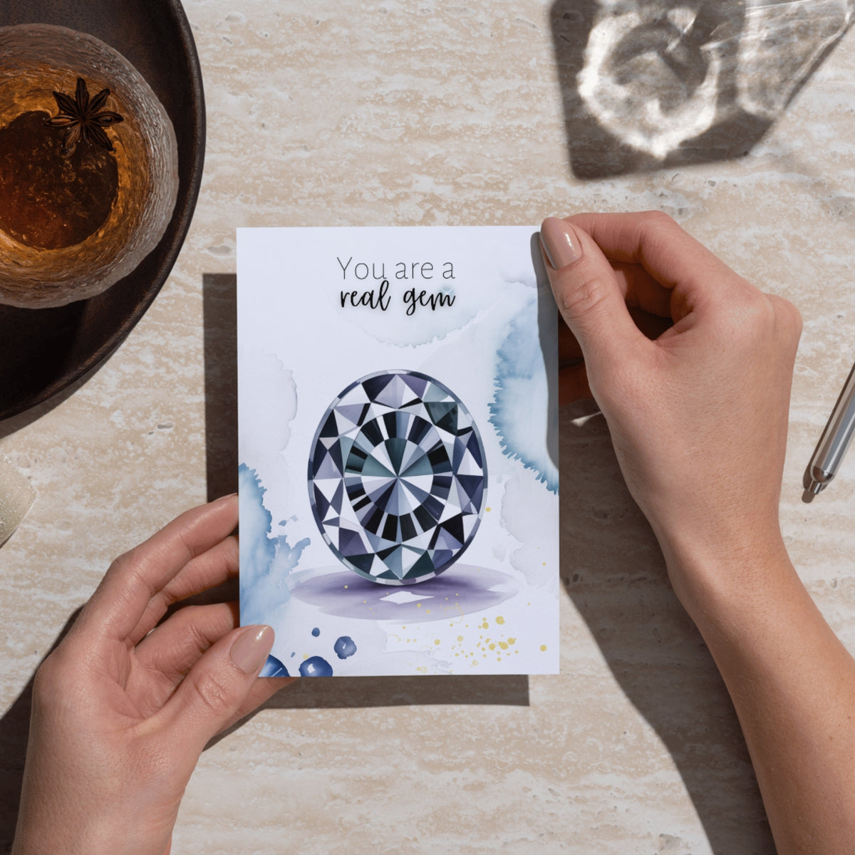 Person holding a card with a oval Spinel Gemstone illustration and text 'You are a real gem' on a table.