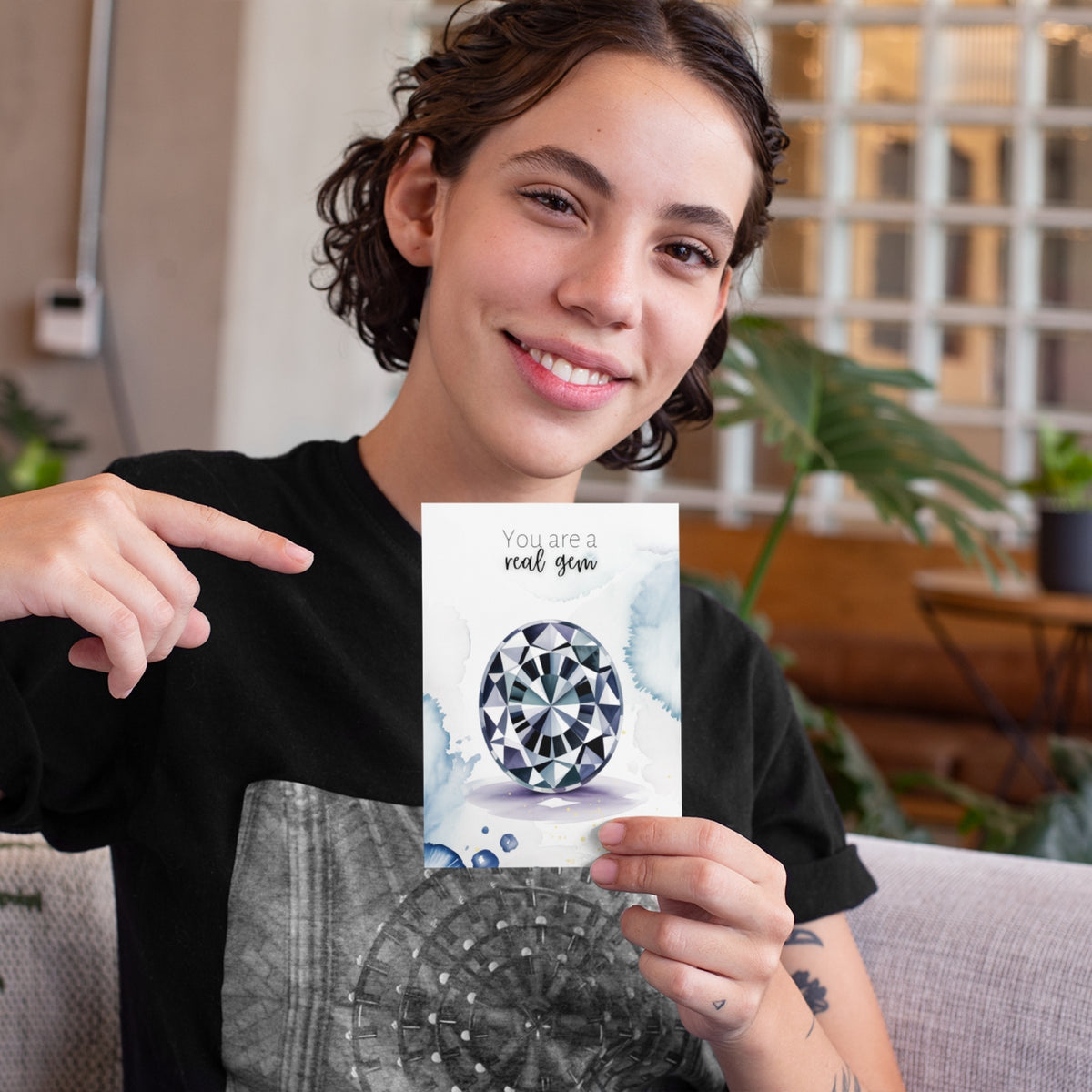 Person holding a card with an oval Spinel Gemstone illustration and text, sitting on a couch.
