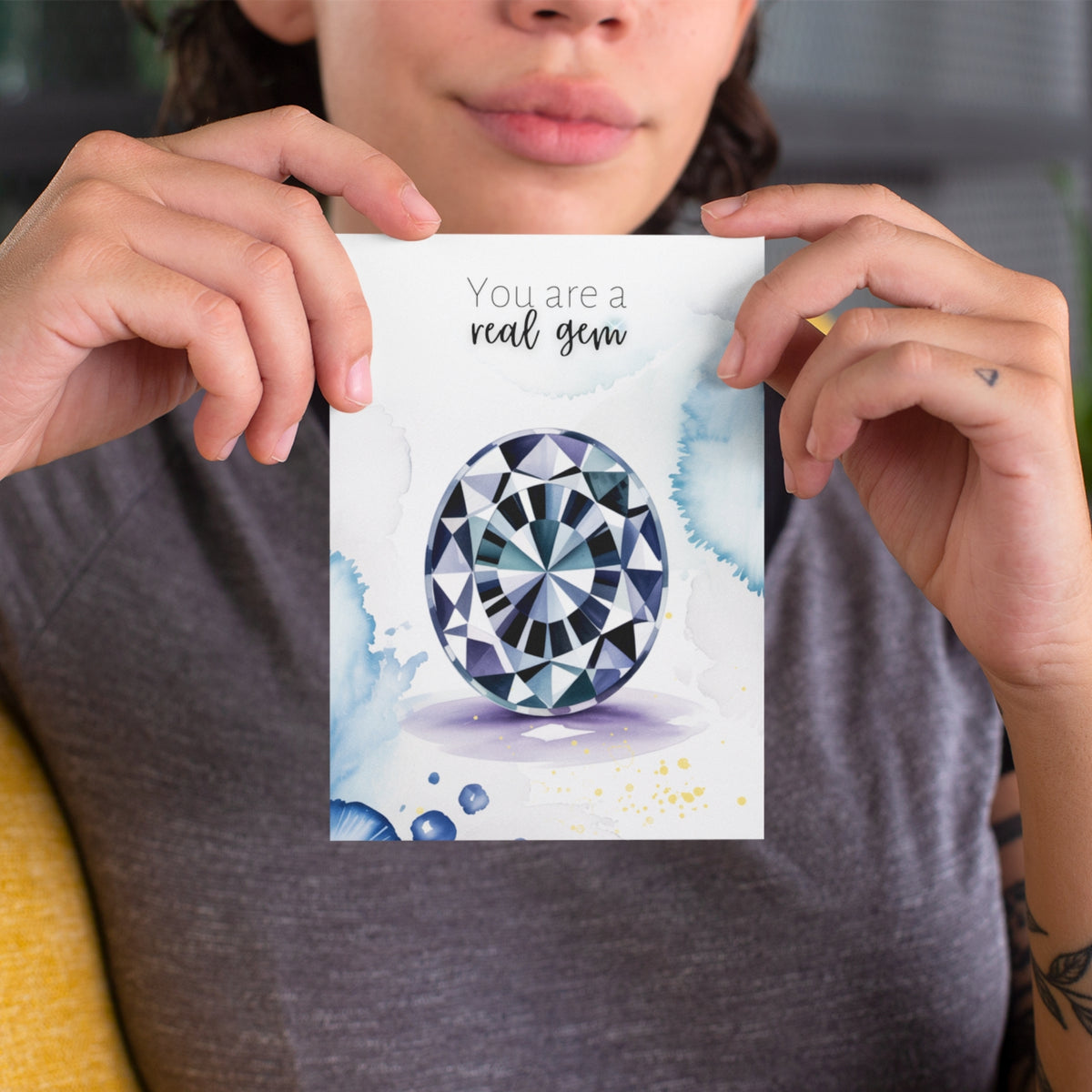 Person holding a card with an oval Spinel Gemstoneillustration and text 'You are a real gem' against a neutral background.