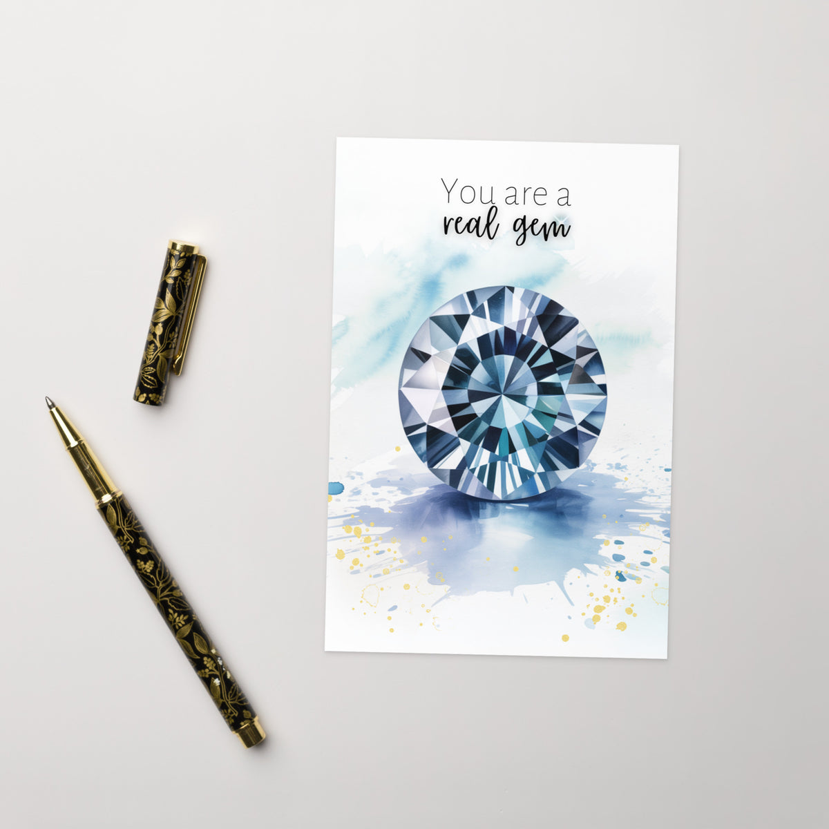 Greeting card with a blue spinel illustration and text 'You are a real gem' on a light gray background, accompanied by a decorative pen.