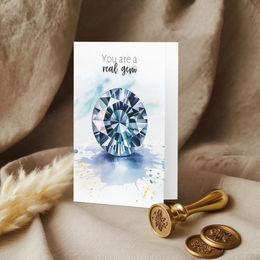 Greeting card with blue spinel illustration and text 'You are a real gem' on a textured surface with decorative elements.
