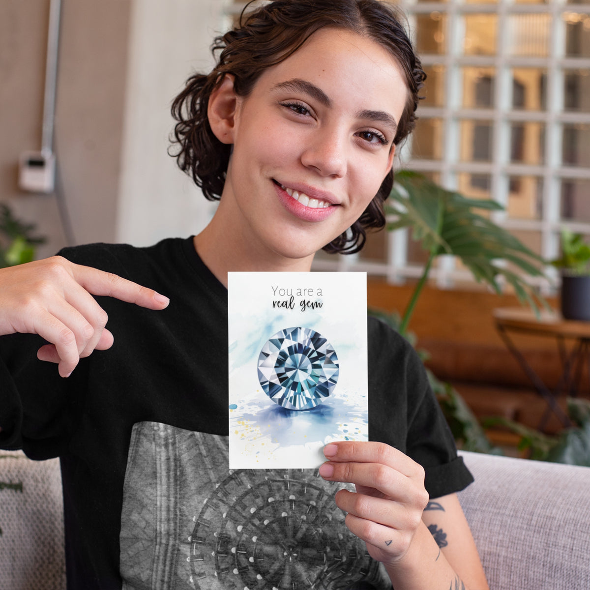 Person holding a card with a decorative watercolor gemstone design and text, sitting on a couch.