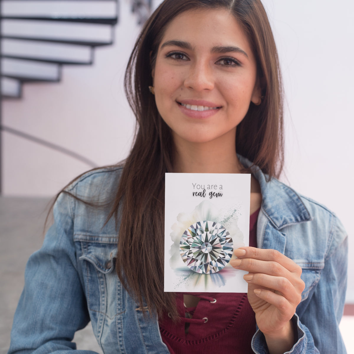 Woman holding a card with a diamond illustration and text, smiling outdoors.