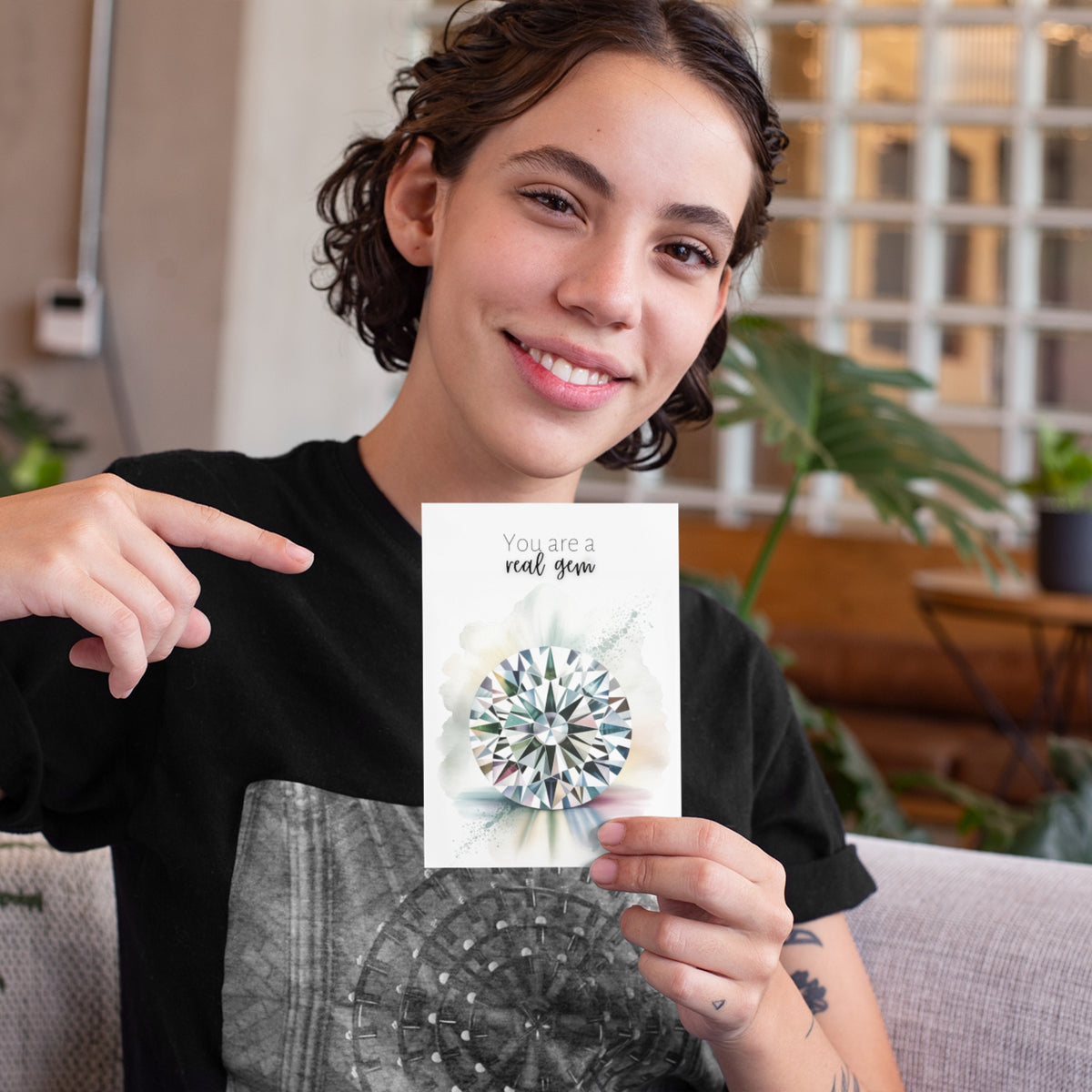 Person holding a card with a decorative diamond illustration design and text, sitting on a couch.