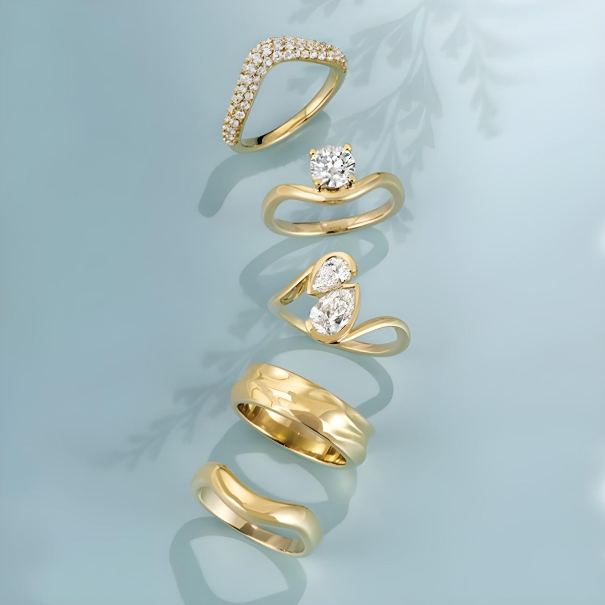 Set of gold rings with diamonds and gemstones on a light blue background