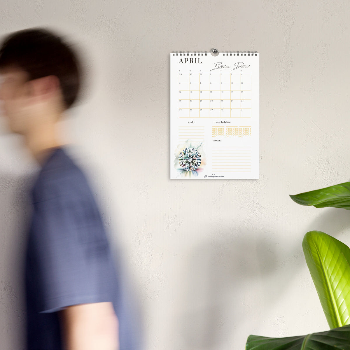 Calendar on a wall with a blurred person and plant in the foreground