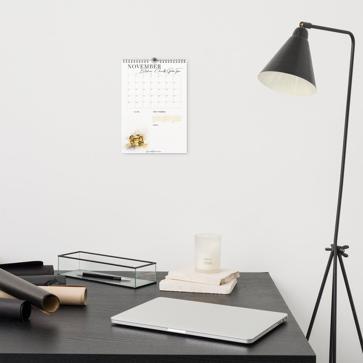 Desk setup with calendar, lamp, and office supplies against a white wall
