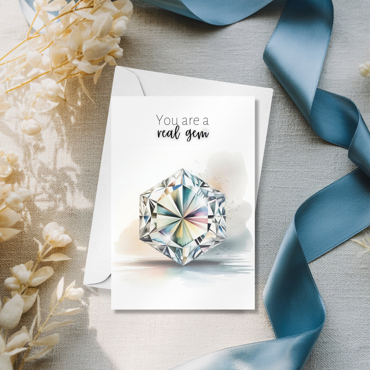 Greeting card with a hexagon diamond illustration and text 'You are a real gem' on a textured surface with flowers and ribbon.