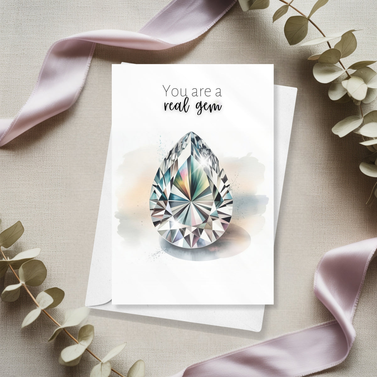 Greeting card with teardrop-shaped gem and 'You are a real gem' text, surrounded by ribbons and leaves on a neutral background.
