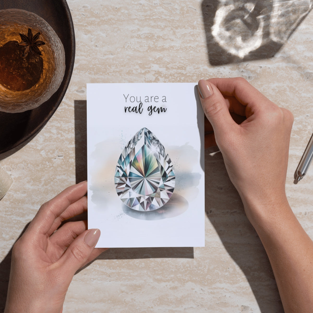 Person holding a card with a diamond illustration and 'You are a real gem' text on a table.