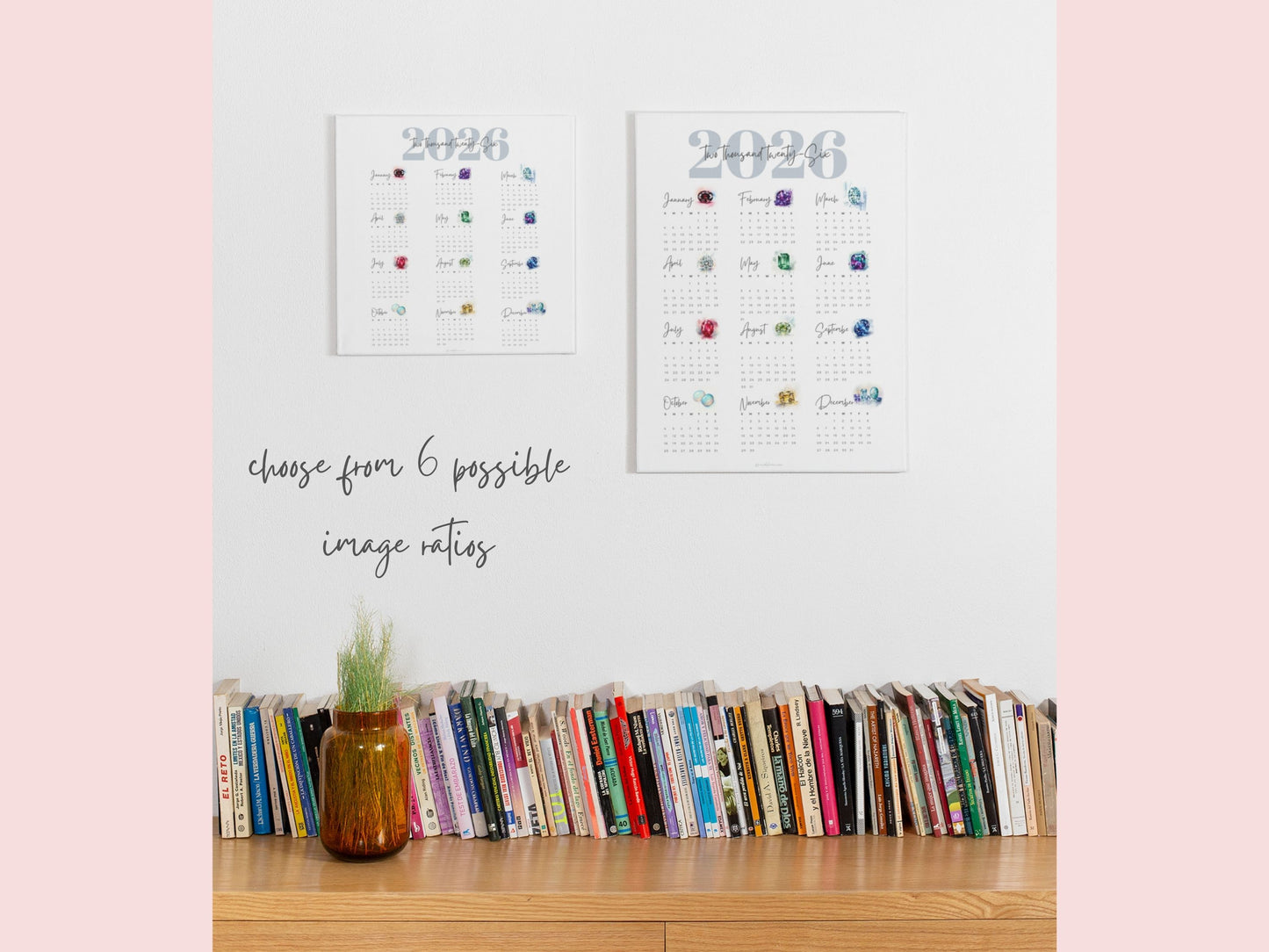 Two 2026 birthstone calendars on a shelf with books and a plant against a light pink background.