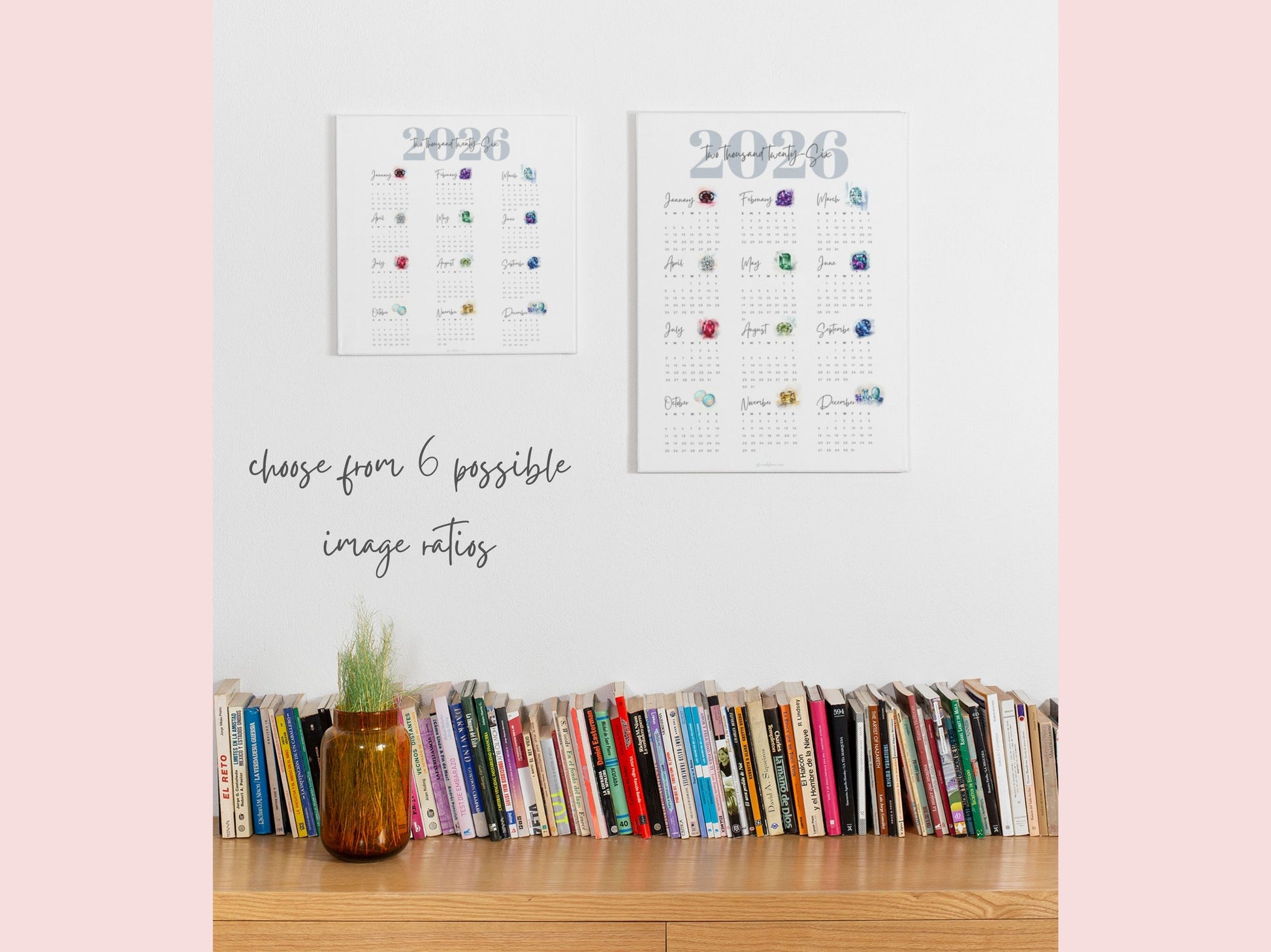 Two 2026 birthstone calendars on a shelf with books and a plant against a light pink background.