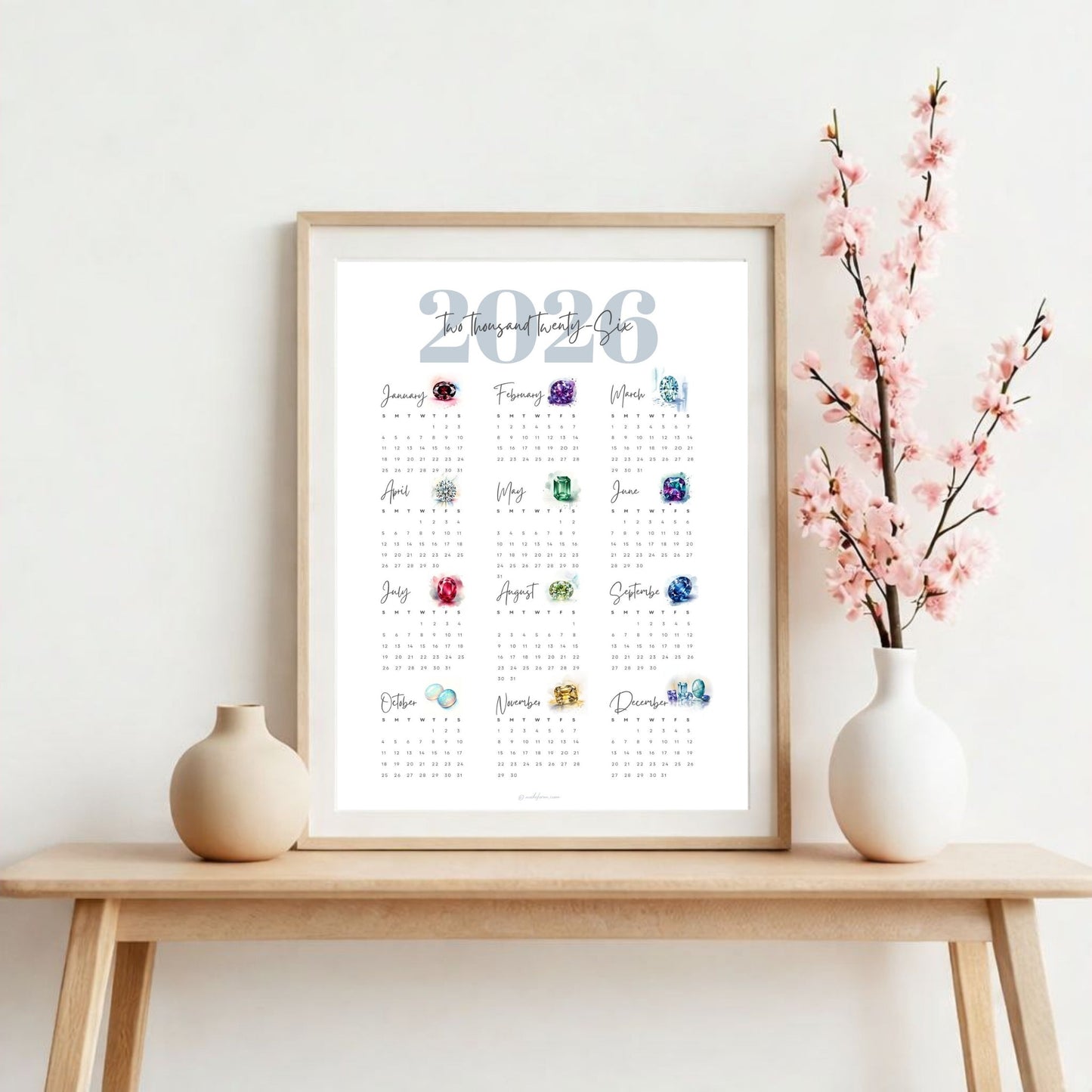 Framed 2026 birthstone calendar on a wooden table with decorative vases and flowers.