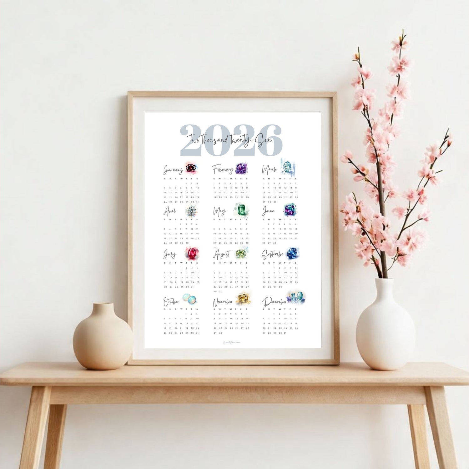 Framed 2026 birthstone calendar on a wooden table with decorative vases and flowers.